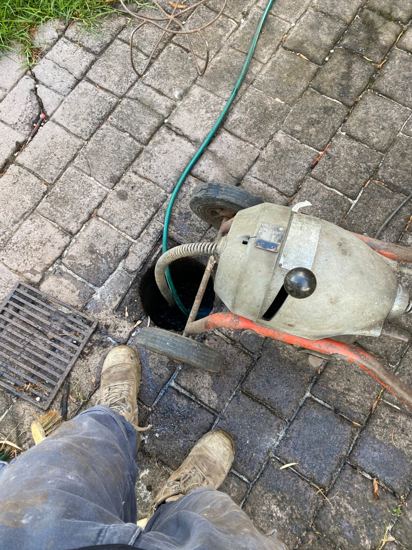 Mechanical drain cleaning machine running a cable into an open drain on paving