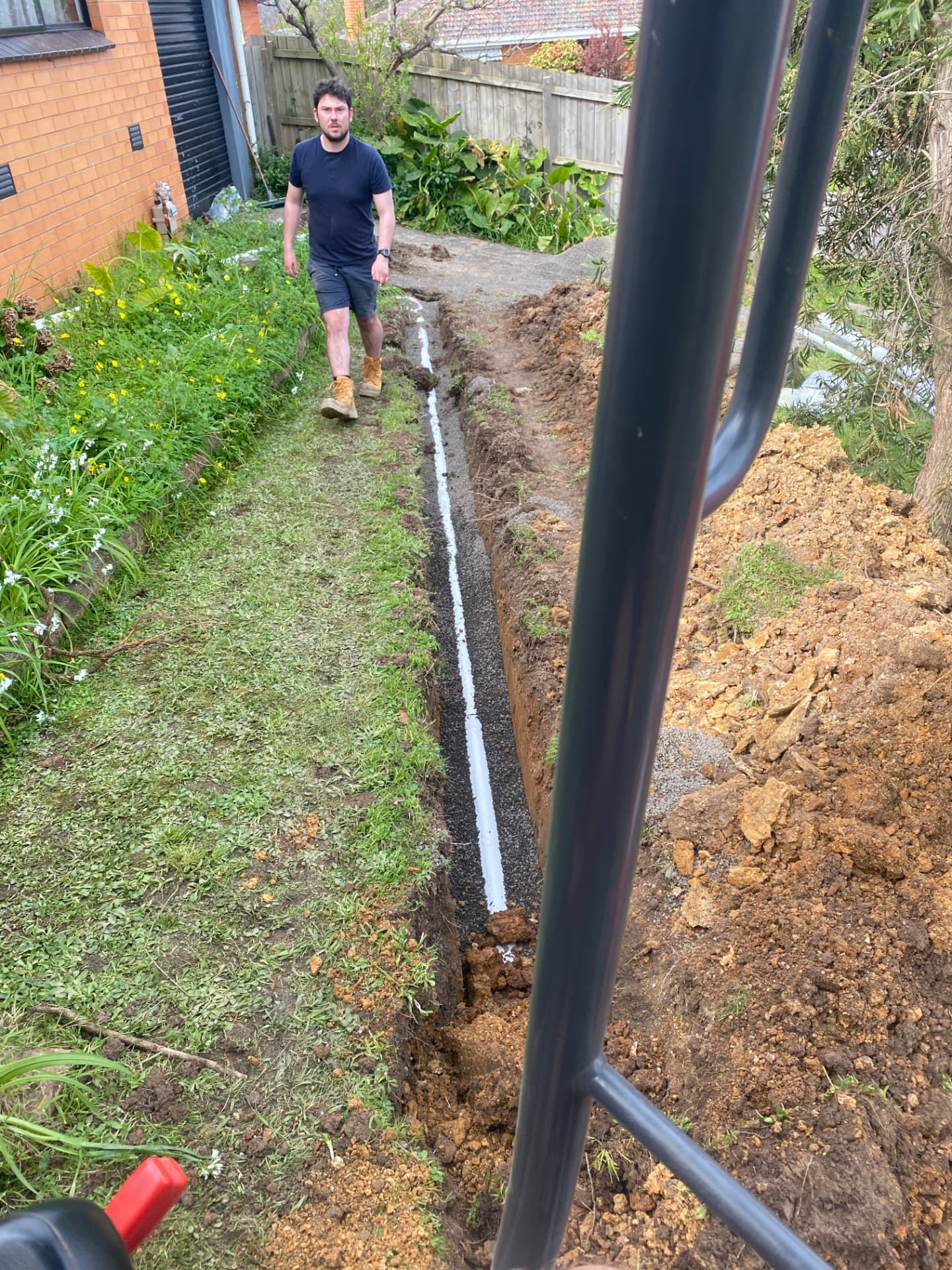 New stormwater pipe bedded in gravel along an excavated trench beside a Melbourne home